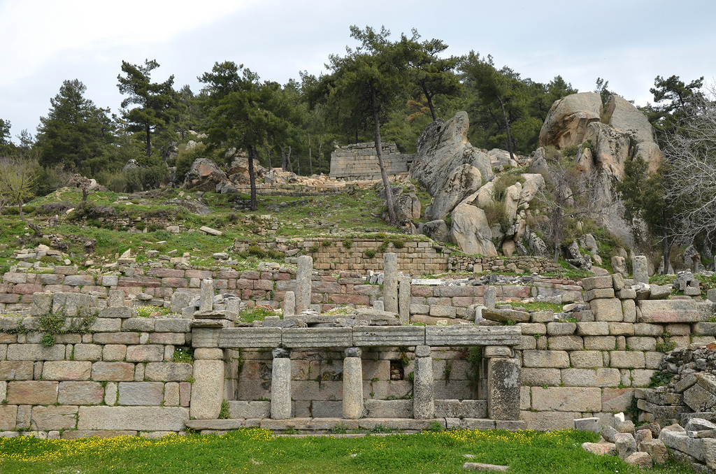 The Well-house with three low gneiss columns with simple Doric marble capitals, note the huge Split Rock in the background which may have been the inspiration for the establishment of the cult to the Carian sky god, Labraunda, Caria, Turkey