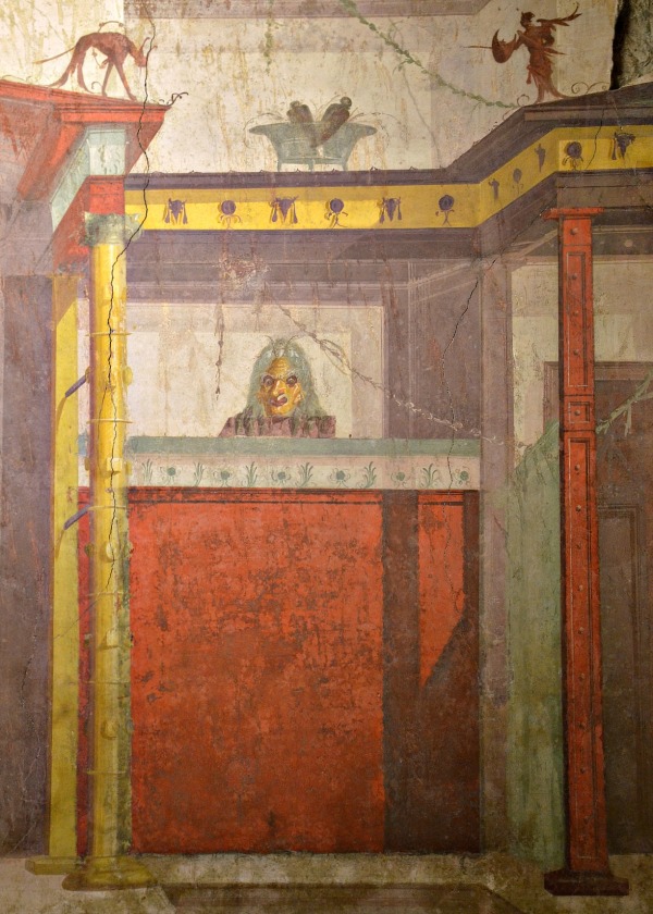 The architecture depicted in the Room of the Masks is a one-storey structure with a central recess and narrow side-doors on each side, probably evoking a scaenae frons, a wooden theatre stage building.